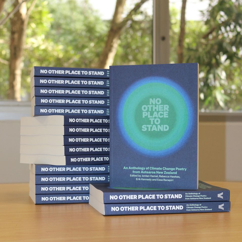 Pile of copies of poetry anthology "No Other Place to Stand" ion table, with trees shown through window in background